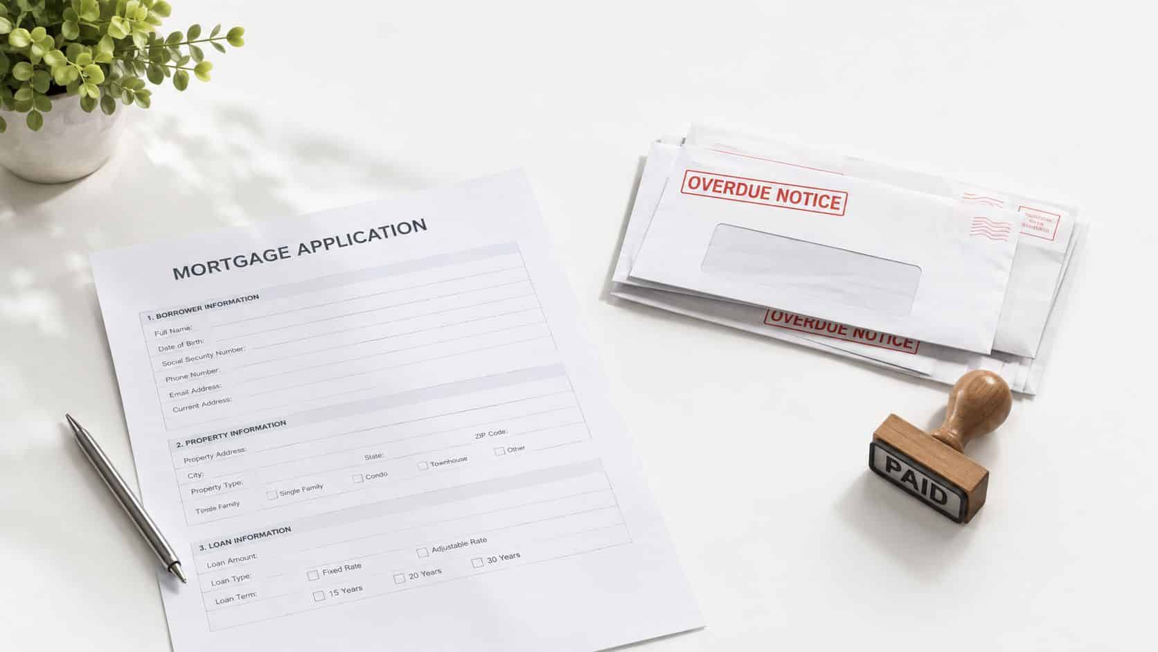 A mortgage application form on a white desk beside overdue notice envelopes and a paid stamp.